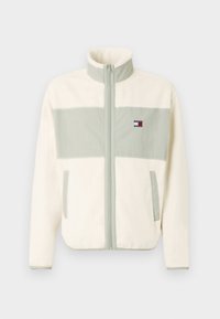 Creme fleecejakke med en lys grøn vandret stribe, høj krave, fuld frontlynlås, to sidelommer og logo-patch på brystet.
