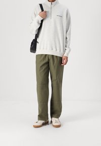 Sudadera de forro polar gris claro con cremallera y logo negro, pantalones cargo verdes oliva y zapatillas blancas con detalles negros. Bolsa de mano cruzada negra.