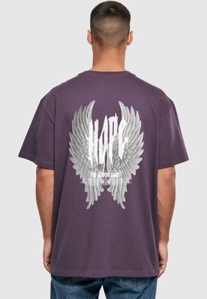 Lilla bomulds t-shirt med løs pasform. Bagsiden prydes af en stor grå grafik af englevinger samt teksten "HOPE THE GUIDING LIGHT." Simpelt design.