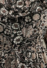 Zwarte bloemenjurk met een gerimpelde halslijn en elastische taille. Opvallend door witte en bruine bloemenpatronen met gedetailleerde versieringen.