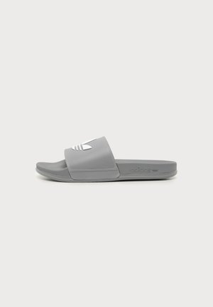 Sandalia de dedo gris de Adidas con logo blanco en la tira, plantilla texturizada y suela plana mostrada de lado.