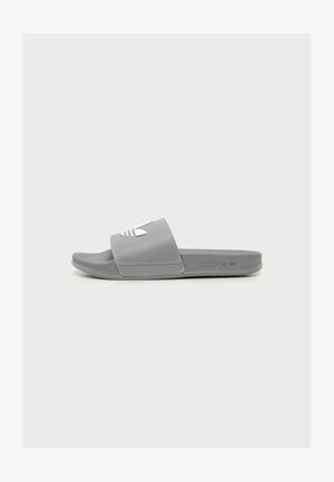 Sandalia de dedo gris de Adidas con logo blanco en la tira, plantilla texturizada y suela plana mostrada de lado.