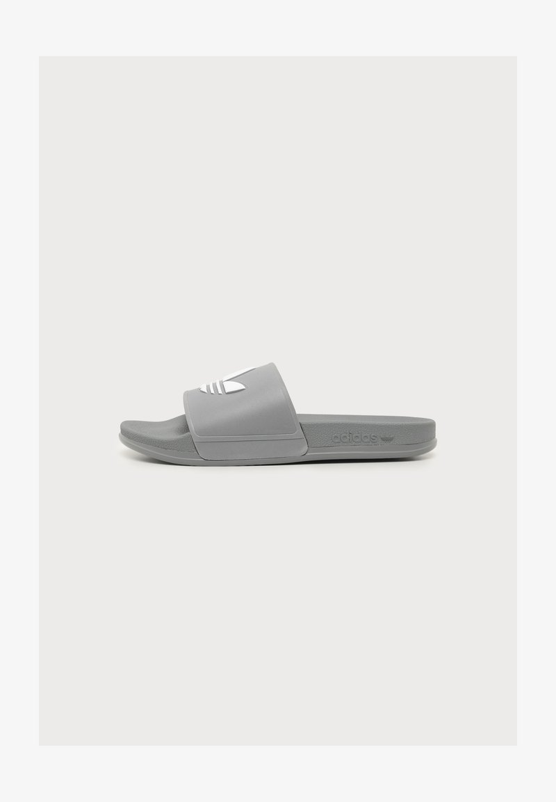 Γκρι σαγιονάρα Adidas με λευκό λογότυπο στο λουράκι, υφή στο πέλμα και επίπεδη σόλα, εμφανίζεται σε πλάγια όψη.