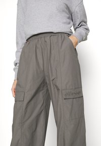 Šedé cargo kalhoty s elastickým pasem, bočními kapsami a vyraženým logem značky. Vyrobeny z lehkého materiálu s volným, širokým střihem.