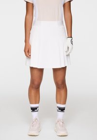 Gonna da golf plissettata bianca realizzata in un tessuto leggero. Indossata con una maglietta chiara, guanti bianchi e sneakers rosa con calzini a strisce bianche e nere.
