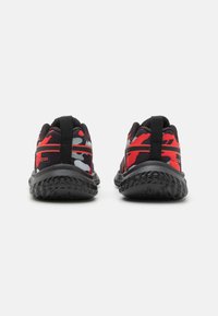 Zapatillas deportivas negras y rojas con un patrón de camuflaje, que cuentan con suelas texturizadas, lengüetas en la parte posterior y una parte superior de malla transpirable.