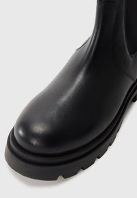 Botte en cuir noir avec un bout rond, des panneaux latéraux élastiques et une semelle en caoutchouc texturée avec des crampons profonds.