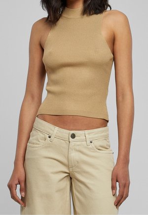 Haut à côtes sans manches en beige clair avec un col montant, associé à un pantalon large beige clair avec une fermeture à bouton à l'avant.