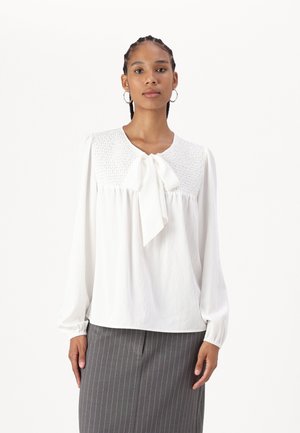 White blouse with a textured smocked yoke and a bow tie at the collar. Long, loosely fitted sleeves. Worn with a pinstriped gray skirt.