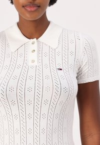 Bijela pamučna polo majica s teksturiranim uzorkom, s malim rupicama, preklopom oko vrata i zatvaranjem na tri dugmeta. Mali logotip na prsima.