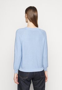 Ljusblå stickad tröja med rund halsringning, raglanärmar och ribbade ärmslut, med ett strukturerat mönster på tyget.