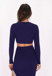 Geribbelde gebreide, cropped marineblauwe trui met lange mouwen en een ronde halslijn, gecombineerd met een bijpassende hooggeritste rok met franjes.
