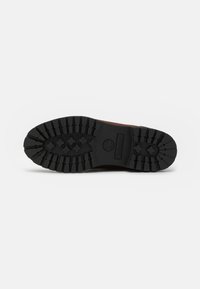 Bruine leren laars met een robuuste zwarte rubberen zool voorzien van diepe groeven en zeshoekige patronen. Timberland-logo in de zool gedrukt.
