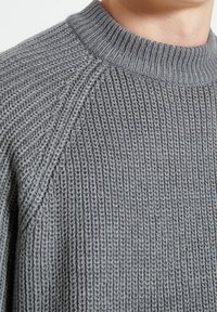 Suéter gris de punto con un cuello alto acanalado y un patrón texturizado, con un corte relajado y mangas raglán.