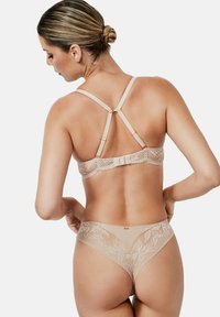 Kanten bh en string set in naaktkleur, met bloemmotieven, verstelbare bandjes en gouden hardware accenten. Soepele textuur en delicate uitvoering.