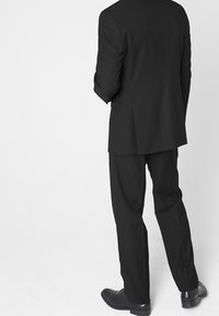 Czarny garnitur z dopasowaną marynarką i prostymi spodniami. Gładka tkanina, minimalne zdobienia. Buty w kolorze czarnym, wypolerowana skóra.