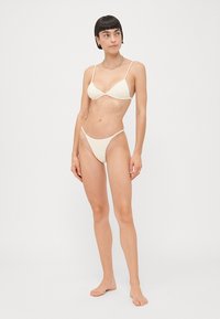 Ivory badpakken set met een triangletop met dunne bandjes en een minimalistische string onderkant. De stof heeft een zachte, matte textuur.