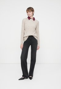 Suéter de punto beige con cuello burdeos oscuro, combinado con jeans negros de campana y bailarinas negras de punta. Diseño simple y ajustado.