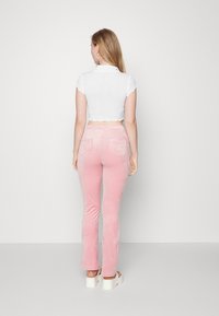 Top branco cropped com bordas onduladas, combinado com calças flared de veludo rosa com bolsos traseiros, usadas com sandálias brancas de plataforma chunky.
