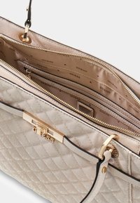 Borsa a tracolla color beige con hardware dorato e dettagli neri. L'interno presenta diversi scomparti, incluso uno con zip.