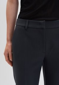 Pantalons gris foncé avec une taille plate, poches avant, texture lisse et coupe ajustée, mettant l'accent sur des lignes épurées.