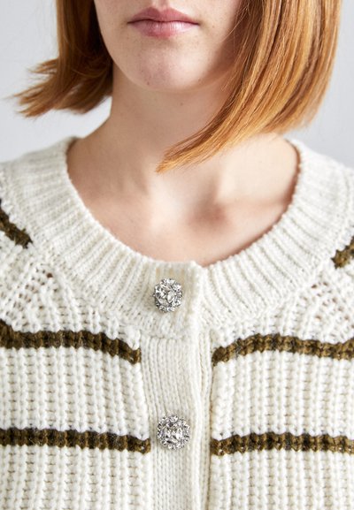 Strikket cardigan i krem med olivenstriper, med en ribbestrikket krage og to dekorative krystallknapper foran. Teksturert stoff.