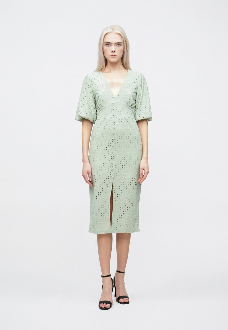 Blomstrete blonder midi kjole i myk grønn med korte pufferm og en frontspalte. Har utskjæringer og en tettsittende silhuett.