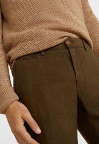 Bruine, gestructureerde broek met een slim fit, voorzien van een knoopsluiting en zijzakken, gecombineerd met een beige gebreide trui.