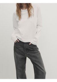 Hvid langærmet skjorte med runde hals, parret med løstsiddende, mørkegrå jeans med høj talje og sidelommer.