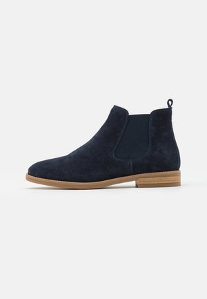 Botte Chelsea en daim bleu marine avec des panneaux latéraux élastiques, une languette à l'arrière, une semelle plate de couleur marron clair et un petit talon empilé.