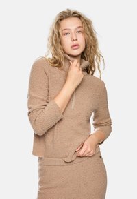 Hellbrauner, flauschiger Pullover mit hohem Kragen und durchgehendem Reißverschluss. Verfügt über lange Ärmel und eine lockere Passform, kombiniert mit einem passenden Rock.
