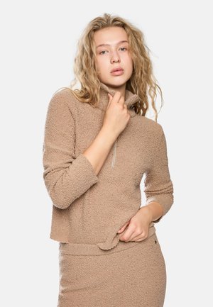 Light brown, fuzzy pullover sweater with a high collar and half-zip closure. Features long sleeves and a loose fit, styled with matching skirt.