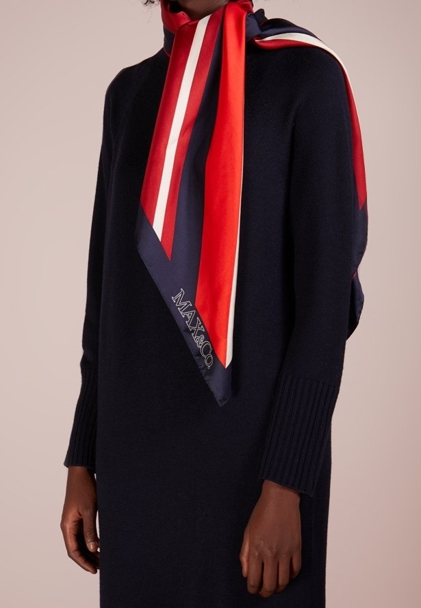 Personne portant une robe en maille à manches longues foncée avec un foulard en soie rayé rouge, blanc et marine noué autour du cou, affichant le texte "MAX&Co".