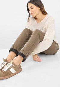 Pantaloni marroni a sigaretta con orli risvoltati, abbinati a sneaker marroni e crema con accenti bianchi e materiali testurizzati. Maglione morbido e leggero.