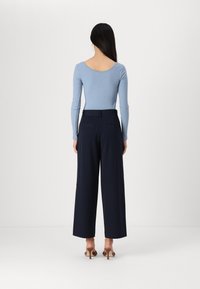 Light blue ribbed long-sleeve top with a scoop back, paired with wide-leg navy pants. Model wears brown heeled sandals, standing against a white background.