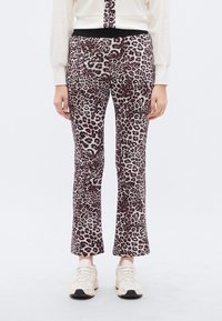 Παντελόνι με λεοπάρ μοτίβο και απαλή υφή, με μαύρη ελαστική μέση, καμπανέ σχήμα, φορεμένο με λευκά αθλητικά παπούτσια.