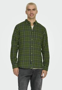 Zielona koszula flanelowa w kratę, z czarno-białymi wzorami, kołnierzykiem zapinanym na guziki oraz jedną kieszenią na piersi. Miękka tekstura, długie rękawy.