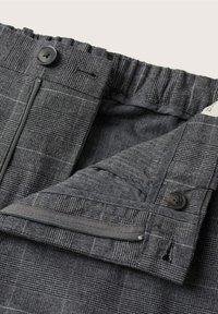 Grijze broek met patroon, voorzien van een elastische tailleband, knoopsluiting, functionele ritsgulp en subtiele textuurvariaties in de stof.