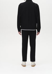 Czarna kurtka i spodnie widziane od tyłu, o prostym kroju. Kurtka ma kołnierz, a spodnie zwężają się przy kostkach.