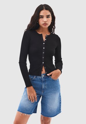 Haut noir à manches longues côtelé avec un devant à boutons, associé à un short en denim bleu clair avec un ourlet effiloché et une coupe décontractée.