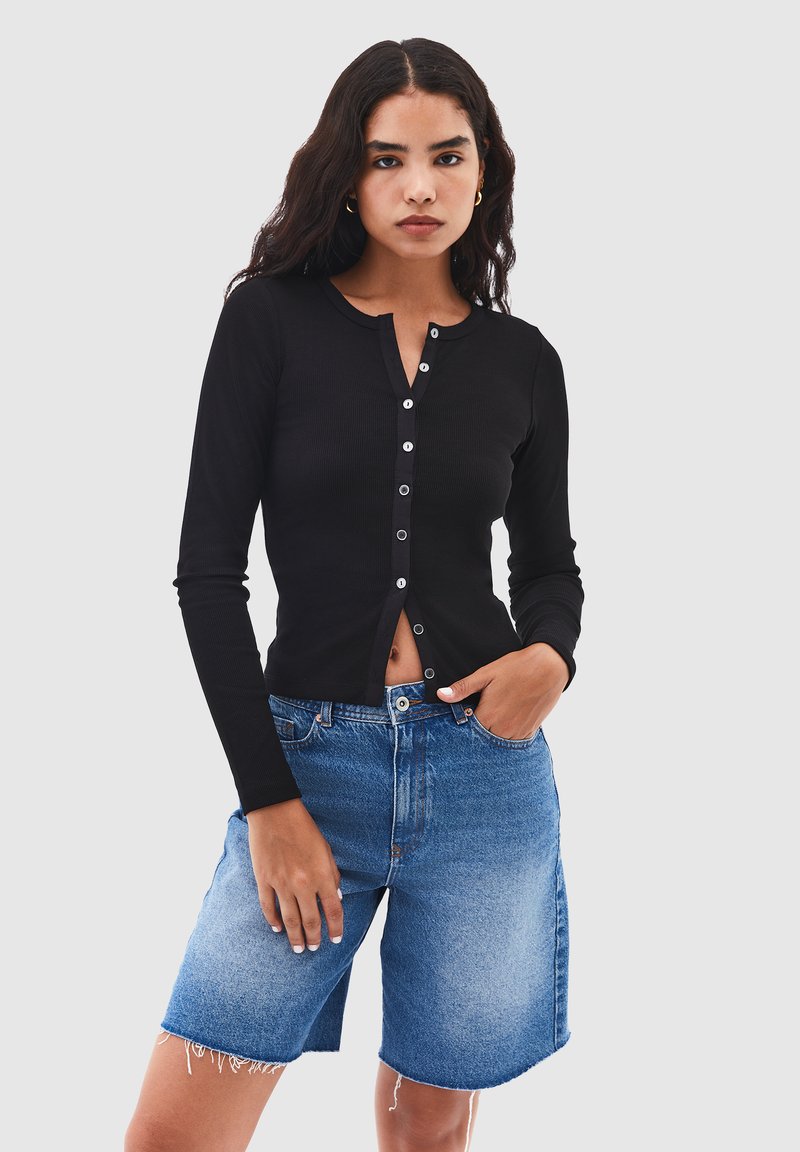 Svart ribbad långärmad topp med knäppning framtill, kombinerad med ljusblå denimshorts med fransar och avslappnad passform.