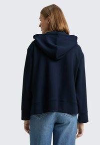 Sweat à capuche bleu marine avec une coupe décontractée, un matériau texturé, une grande capuche et des poignets côtelés. Associé à un jean en denim délavé.