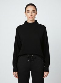 Maglione nero a collo alto in maglia con maniche lunghe, vestibilità morbida, polsini a coste e una texture liscia. Indossato con pantaloni neri con coulisse.