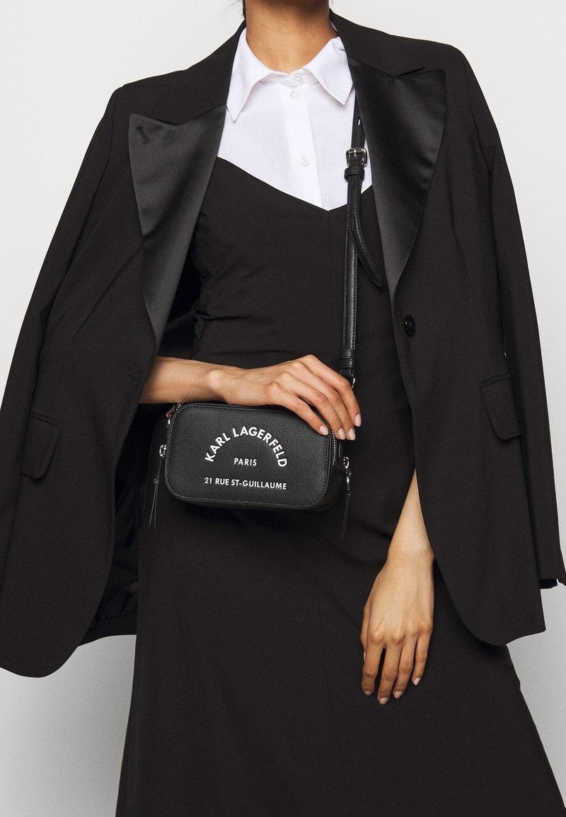 Czarna skórzana torba na ramię z białym napisem "KARL LAGERFELD PARIS" oraz "21 RUE ST-GUILLAUME". Posiada zamki błyskawiczne i dekoracyjne chwosty.