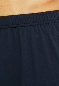 Cintura elastica di pantaloni corti in cotone blu navy, texture liscia, con una cucitura arricciata per il comfort e una vestibilità rilassata.