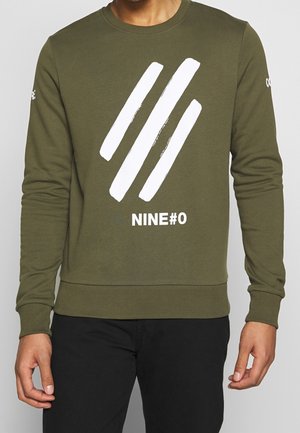 Olive green sweatshirt, cotton fabric, crew neck. Features white graphic design with diagonal stripes and text "NINE#0" on the front.