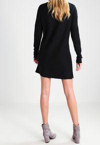 Svart stickad klänning med långa ärmar, sidofickor och en avslappnad passform, parat med grå ankelstövlar. Mjuk textur och enkel design.