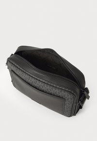 Sacoche en bandoulière noire avec une finition en cuir lisse, détail en motif logo texturé, fermeture à double zip et une bandoulière réglable pour le confort.