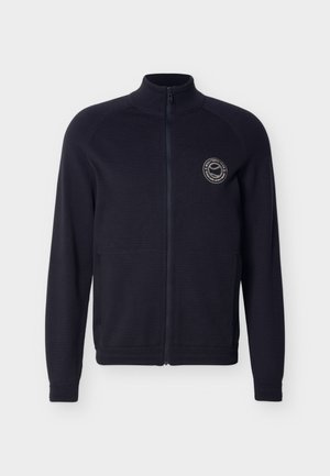 Veste zippée intégrale bleu marine avec col montant, deux poches avant et petit logo circulaire sur la poitrine gauche.