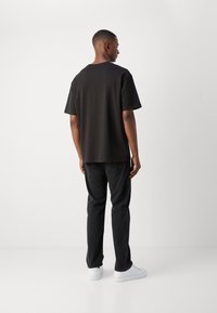 Sort kortærmet t-shirt med en afslappet pasform, parret med mørke jeans og hvide sneakers. Glat stof, enkelt design, ingen mønstre eller accenter.